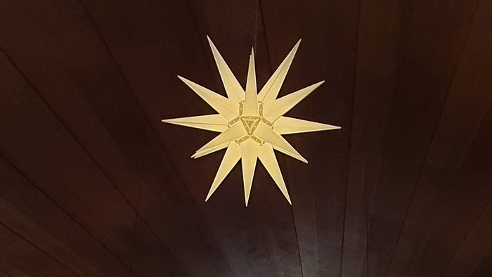 Ein großer, gelber Stern hängt an einer dunklen Holzdecke.