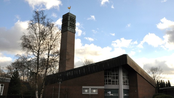 Gebäude mit hohem Turm und goldener Spitze, umgeben von Bäumen unter blauem Himmel