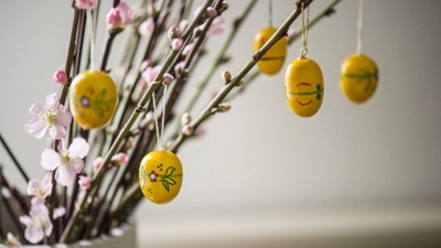 Dekorative gule påskeæg og blomstrende grene i en vase med glade emoji-stil ansigter.