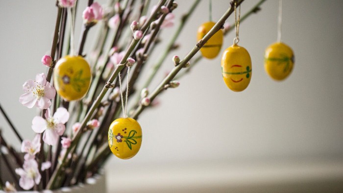 Dekorative gule påskeæg og blomstrende grene i en vase med glade emoji-stil ansigter.