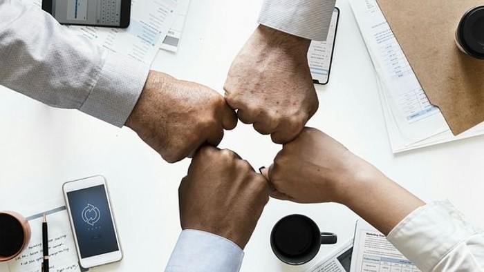 En gruppe af medarbejdere slår fister sammen over et kontor med papirer og telefoner.