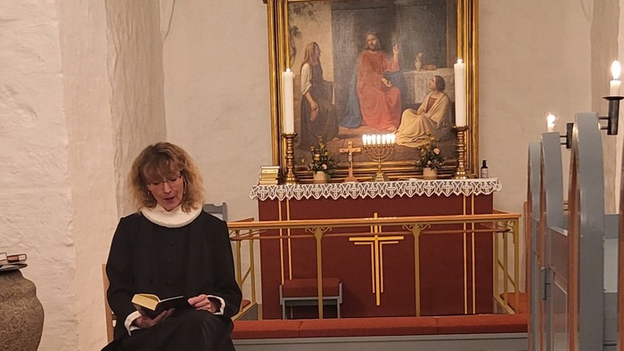 En kvinde i mørkt kapittel sidder i en kirke foran et alter med lys.