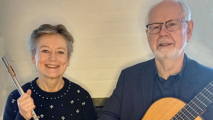 To glade musikere, der holder en fløjte og en akustisk guitar, poserende sammen indendørs.