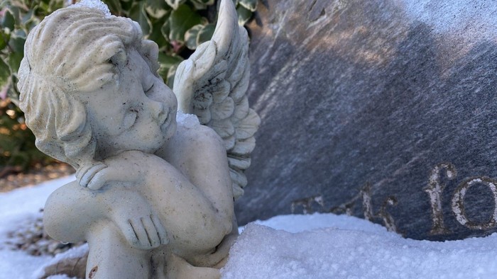 En kerubstatue med udbredte vinger hviler på en snedækket overflade ved siden af et stort stenur.