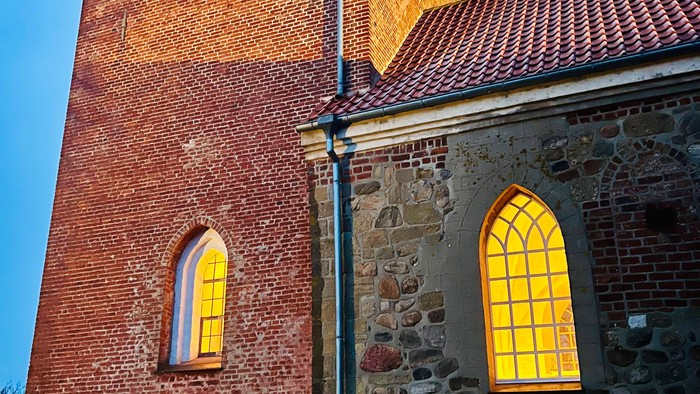 Røde mursten og sten på kirke med høje tårn.