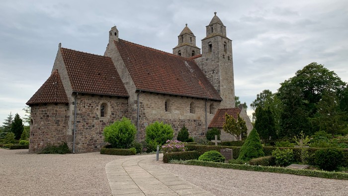 Gammel kirke med spistegn og klokketårn i trædiget landskab