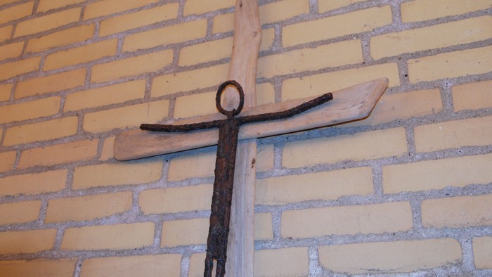 En trækorsfigur hænger på en mur af gule mursten.
