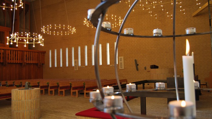 En kirkeindendels med lysende lys og lysstake, med bænke og lysestage.