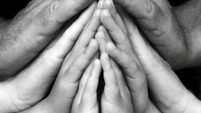 En sort-hvid fotografi af flere håndflader, der er lagt sammen i en pyramideform.