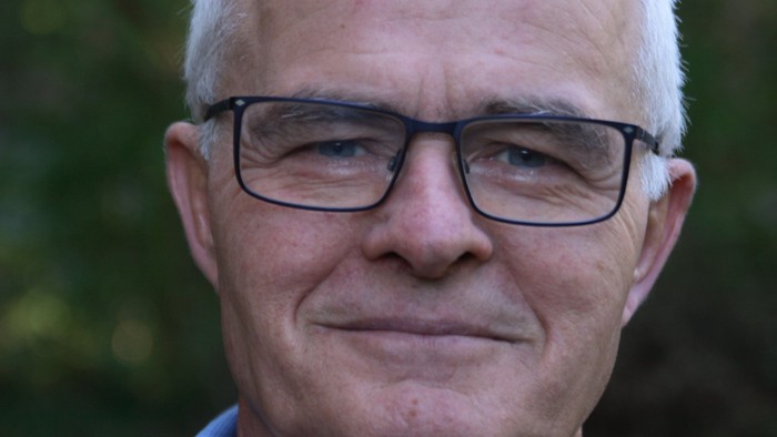 En smilende, eldhåret mand med briller og blå jakke.