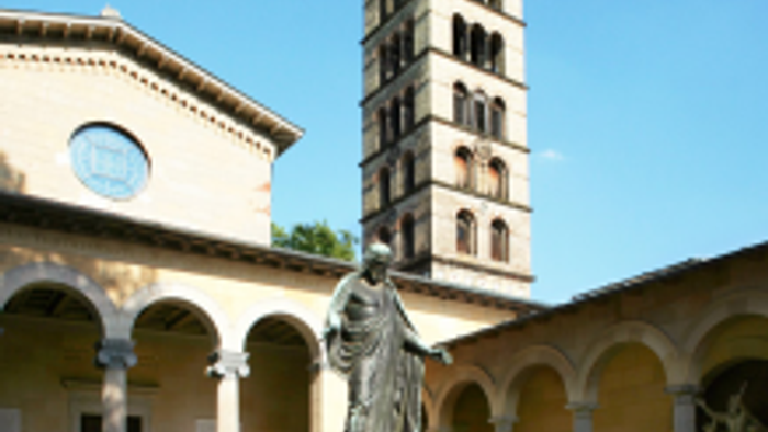 Im Innenhof einer Kirche steht eine Statue vor einem hohen Turm.
