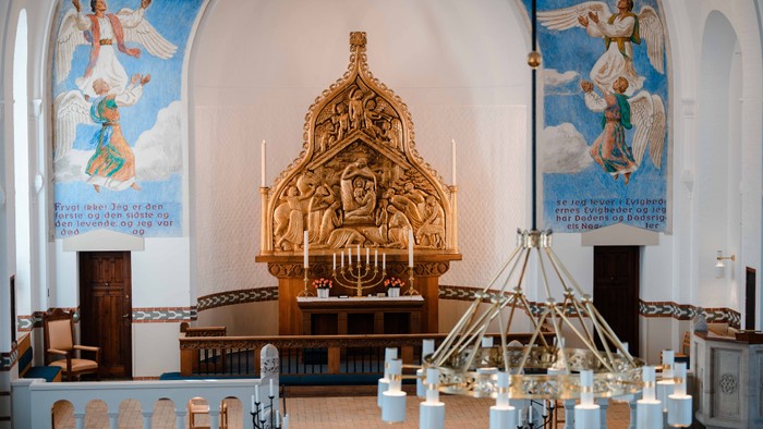 Indre del af kirke med alter, lysestager og malerier.