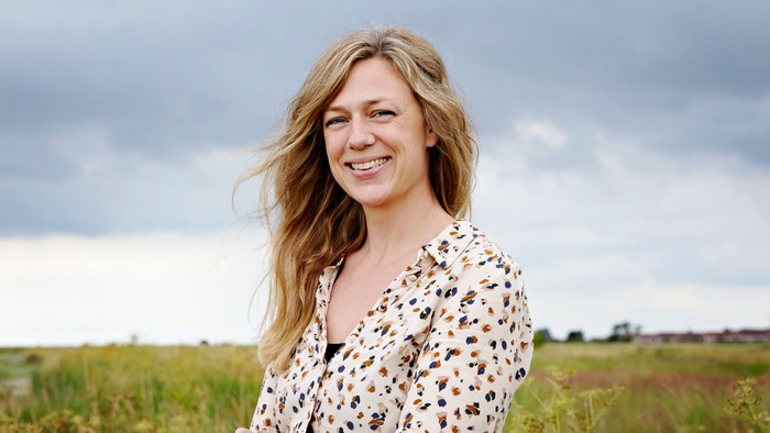 En kvinde med blond hår står i et grønt felt og smiler til kameraet.