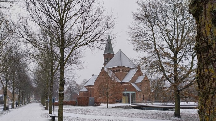 En snedækket park med en mørk teglsteinskirke med spisse tårn.