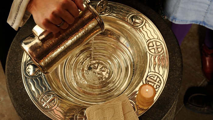 En person tømmer en flaske med væske i en stor, dekoreret badekar.