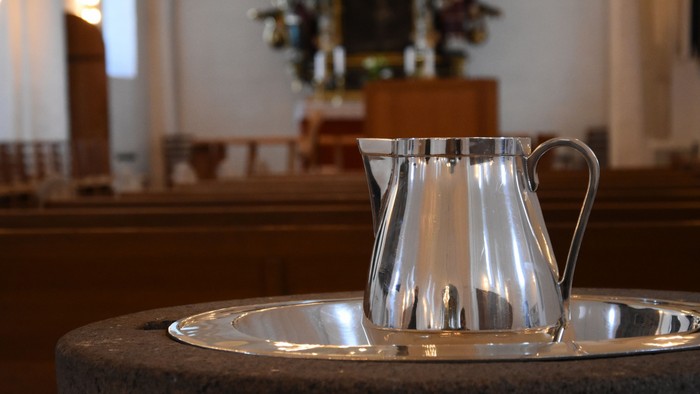 En sølv kaffe-kanne står på bord i kirke.