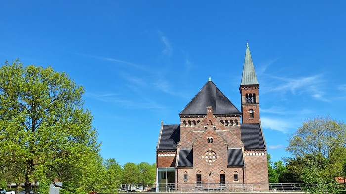 Et rødt teglkirke med spiret mod himlen og træer foran