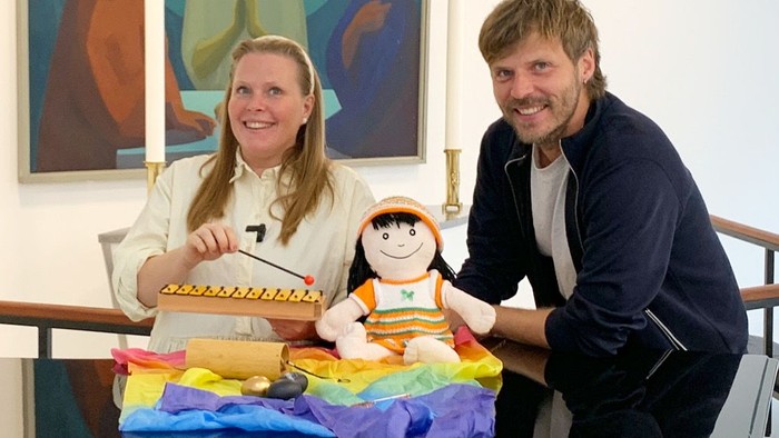 En mand og en kvinde sidder med en dukke og en regnbueflag.