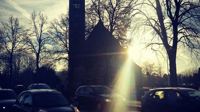 En kirke med tårn og solskin bagved.