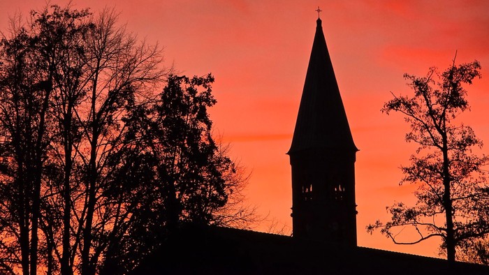 En kirke med tårn mod en rød solgangshimmel