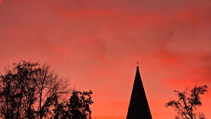 En kirke med tårn mod en rød solgangshimmel
