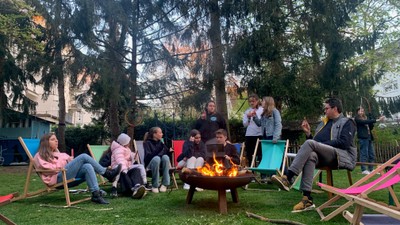 Eine Gruppe versammelt sich um eine Feuerstelle im Freien in einem Park und sitzt auf bunten Gartenstühlen.