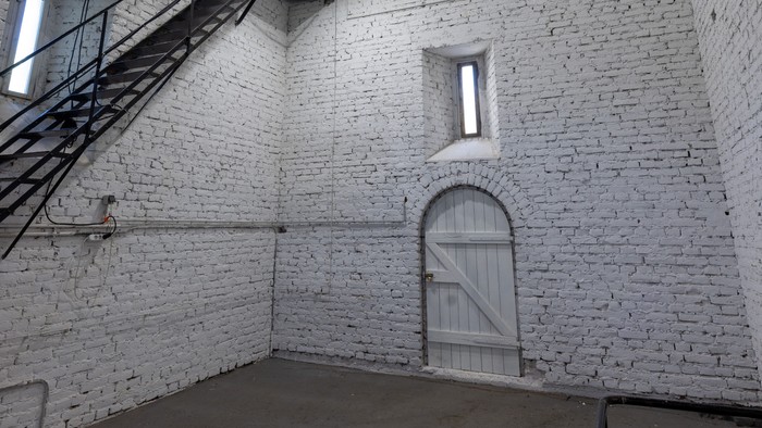 Industrieller Raum mit Wendeltreppe, Rundbogentür und minimalistischer Beleuchtung an weiß getünchten Wänden.