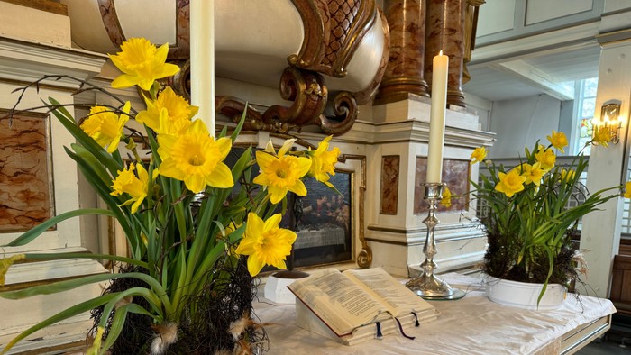 Eleganter Altar, geschmückt mit leuchtend gelben Osterglocken, Kerzen und einem offenen Buch auf einem verzierten Tisch.