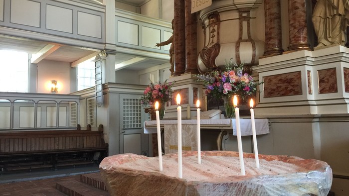 In der Kirche stehen drei brennende Kerzen auf einem Tisch mit Blumen.