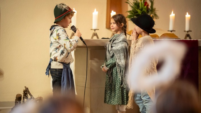 Kinder treten auf einer Bühne auf, während es sich offenbar um eine festliche oder religiöse Veranstaltung handelt.
