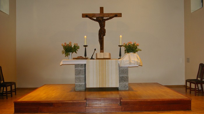Das Bild zeigt einen Altar mit einem Kruzifix und Kerzen in einer Kirche.
