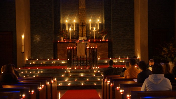 In der Kirche sitzen Menschen bei Kerzenschein vor dem Altar.