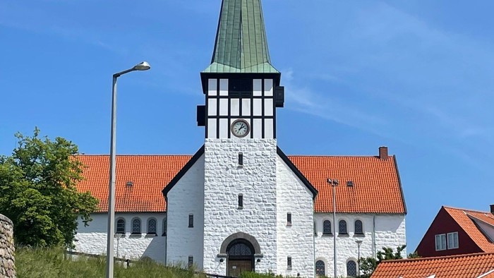 En hvid kirke med spiret og klokke, omgivet af andre huse med røde tag.