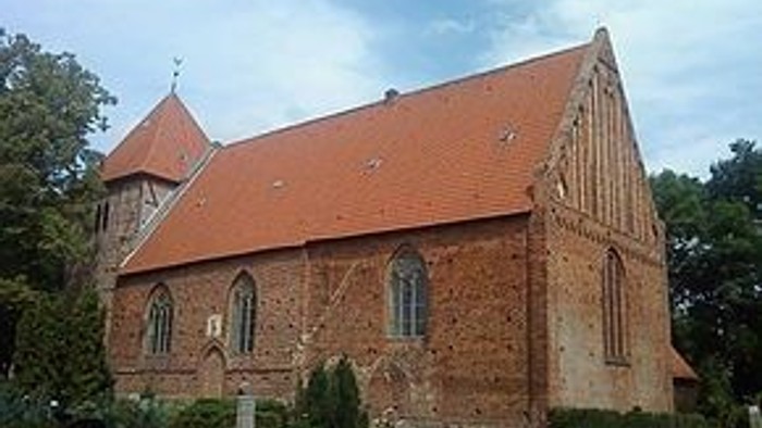 Das Bild zeigt eine alte Kirche mit rotem Dach und einem kleinen Friedhof.