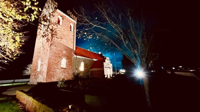 Natlys af en oplyst murstensbygning med et træ og lys foran