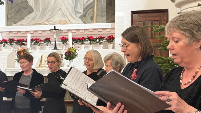 En gruppe kvinder, der synger sammen i en udsmykket kirke under en kormusikopførelse.