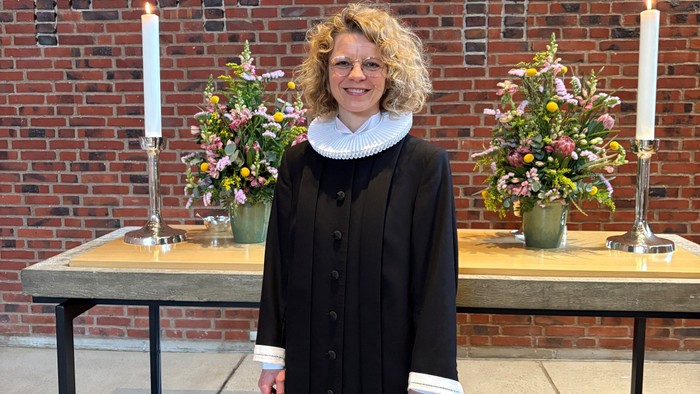 Kvinde i sort kjole, der står foran en murstensvæg med borde og stearinlys.