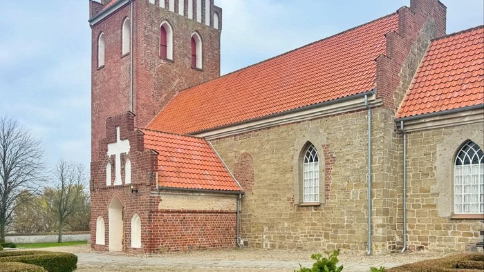 Historisk stenkirke med rødt tag og højt tårn.