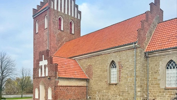 Historisk stenkirke med rødt tag og højt tårn.