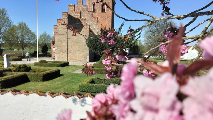 En dansk flagvåben ved en slottsagtig bygning med blomster i forgrunden