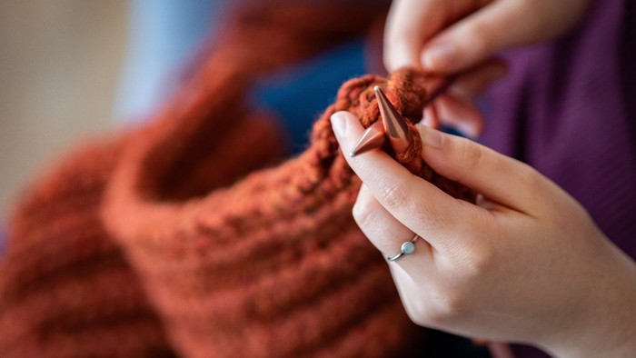 En person laver strømpe med rødt garn.