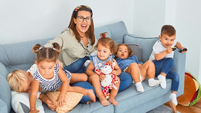 Eine Mutter sitzt mit ihren vier Kindern auf einem blauen Sofa in einem hellen Raum.