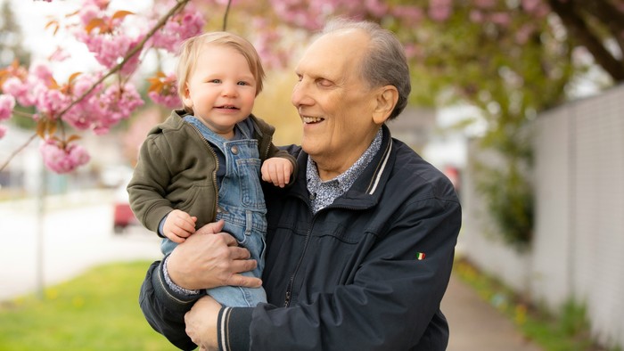 Ein älterer Mann hält ein Baby unter einem blühenden Baum.