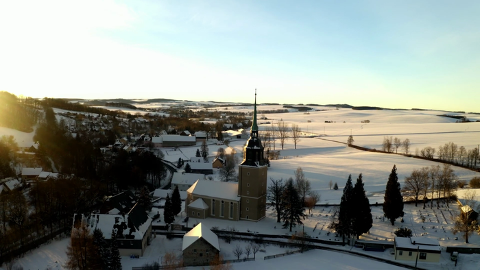 Schneebedeckte Landschaft mit Dorf und Kirche bei Sonnenuntergang