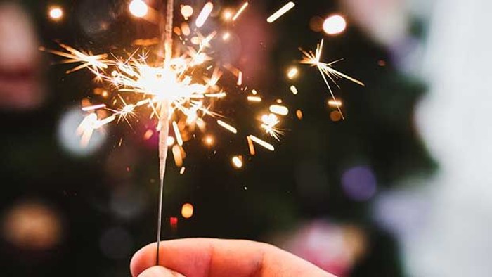 En hånd holder en lyse sparkler med glitrende funker i mørket.