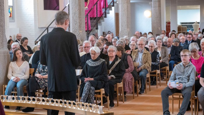 En gudstjeneste med en præst, der leder menigheden i en kirke, hvor de holder lys på en rækværk.