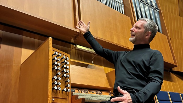 En mand spiller på et orgel med udtryksfulde bevægelser i en stor trækirke.