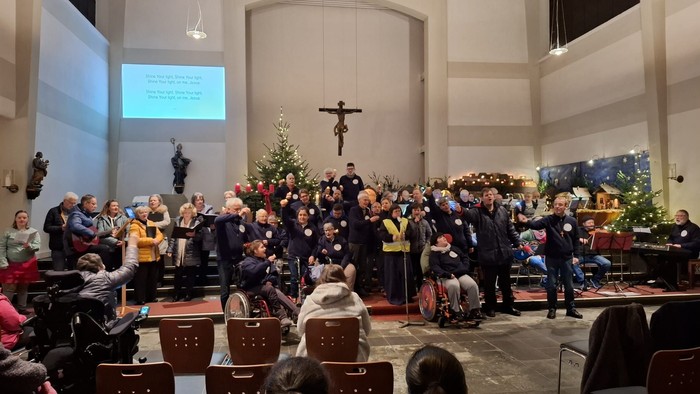 Große Kirche. Blick aus den Kirchenbänken, in den Menschen sitzen, zum Altarraum, in dem der Chor versammelt ist. Der ganze Altarraum ist voll.