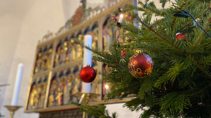 En juletree med røde kugler foran en prædikestol med udsmykning