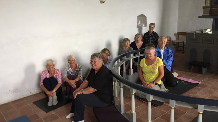 En gruppe ældre personer sidder på bænke i kirke.